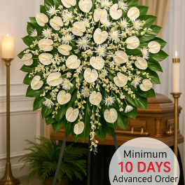 Large white standing funeral spray with heart-shaped blooms and dark green leaves on an easel before a casket