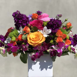 Bright mixed bouquet with roses, orchids, and purple blooms in a white vase