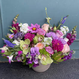 Mixed bouquet of pink, purple, white, and green flowers in a round vase