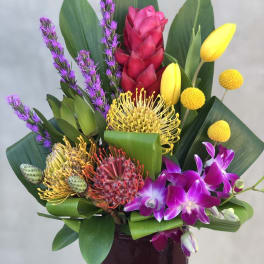Tropical bouquet with orchids, pincushion protea, and yellow tulips in a vase