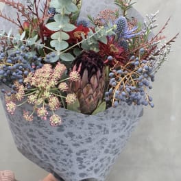 Mixed bouquet with a protea, blue berries, and eucalyptus in gray wrap