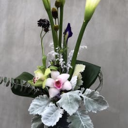 Tall floral arrangement with white calla lilies and orchids in a dark vase