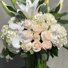 White lilies and pale roses arranged in a tall glass vase