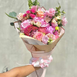Handheld bouquet of pink and peach roses with mixed blooms wrapped in paper