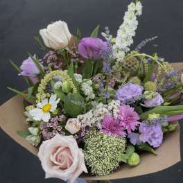 Mixed bouquet of pink, purple, and white flowers wrapped in brown paper