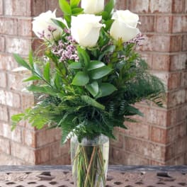 White roses arranged in a clear glass vase with greenery