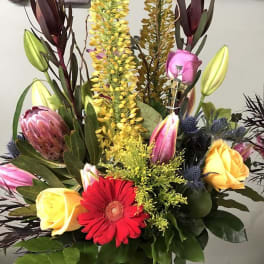 Tall mixed bouquet in a green vase with roses, lilies, and a red gerbera daisy