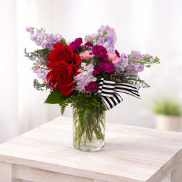 Bouquet of red and pink flowers in a clear glass vase with a striped ribbon