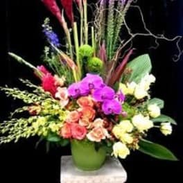 Tall mixed floral arrangement in a green vase with pink, purple, and white blooms