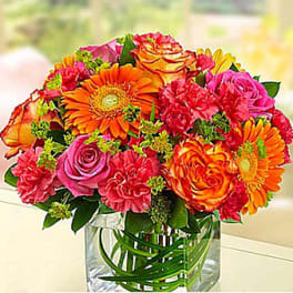 Bright mixed bouquet of orange, pink, and yellow flowers in a clear vase