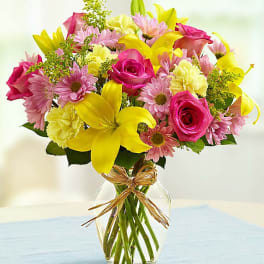Bouquet of pink roses, yellow lilies, and daisies in a glass vase