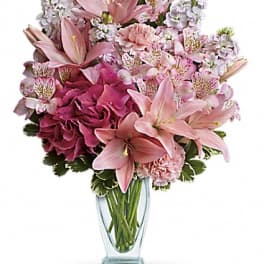 Pink lilies and mixed pink flowers in a clear glass vase