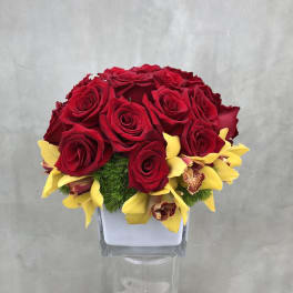 Red roses with yellow orchids in a clear square vase