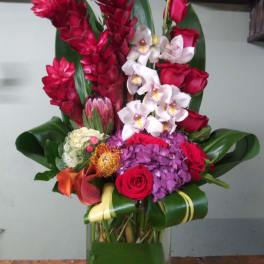 Tall tropical bouquet with red roses, white orchids, and purple hydrangea in a glass vase