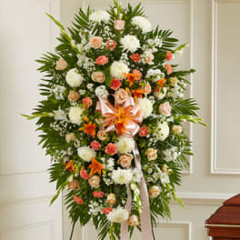 Standing floral spray with white, peach, and orange flowers on a ribboned easel
