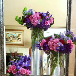 Three purple and pink floral arrangements in tall glass vases