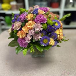 Mixed bouquet of purple, pink, yellow, and peach flowers in a glass vase