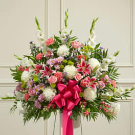 Large standing floral spray with pink, white, and purple flowers and a bright pink ribbon