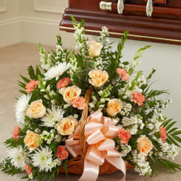 Basket arrangement of peach and white flowers with a pink ribbon