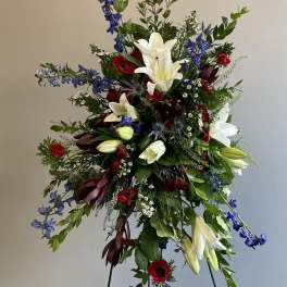 Tall floral spray with white lilies, red blooms, and blue flowers on a stand