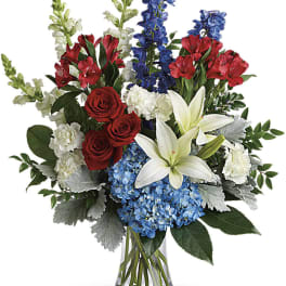 Red roses, white lilies, blue hydrangeas, and red alstroemeria in a glass vase