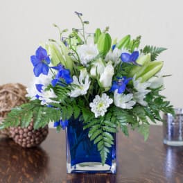 Blue vase with white and blue flowers and green foliage