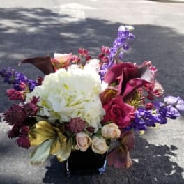 Bouquet of white hydrangea, roses, and purple flowers in a black vase