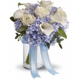White roses and calla lilies with blue hydrangeas in a glass vase with ribbon