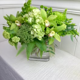 Green floral arrangement in a glass vase with orchids and hydrangeas