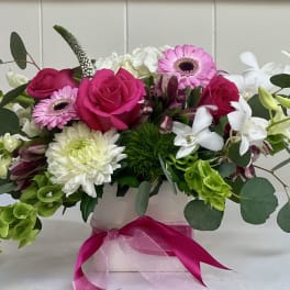 Pink and white mixed flower arrangement in a white vase with a pink ribbon