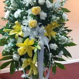 Standing floral spray with yellow lilies, white roses, and a white ribbon