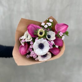 Bouquet of pink calla lilies and white anemones wrapped in brown paper