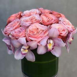 Pink roses and lavender orchids arranged in a green glass vase