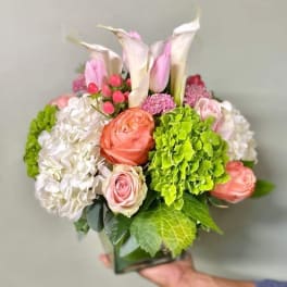 Bouquet of pink calla lilies, roses, and hydrangeas in a square vase