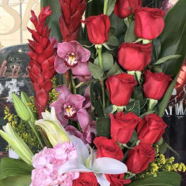 Tall arrangement of red roses, orchids, and pink flowers in a black vase
