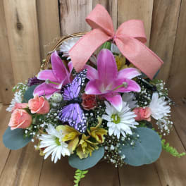 Basket arrangement with pink lilies, white daisies, and a pink bow