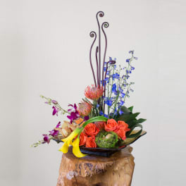 Tall floral arrangement with orange roses, blue orchids, and yellow calla lilies