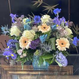 Mixed bouquet of blue, purple, and cream flowers in a glass vase