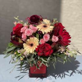 Red and pink rose bouquet with gerbera daisies in a red vase