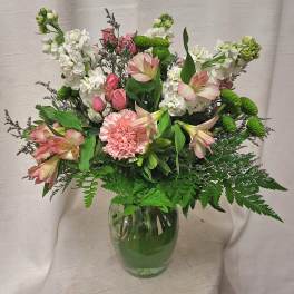Mixed bouquet of pink and white flowers with green accents in a clear glass vase