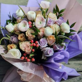 Pastel bouquet of roses and ranunculus wrapped in lavender paper