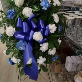 Standing floral spray with blue and white carnations and a purple ribbon
