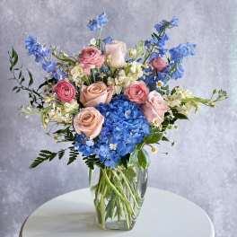 Pink roses and blue hydrangeas arranged in a clear glass vase