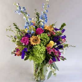 Mixed bouquet in a clear glass vase with blue, pink, yellow, and purple flowers