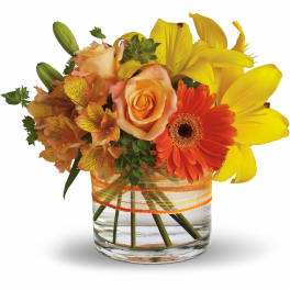 Orange roses, yellow lilies, and a gerbera daisy in a glass vase