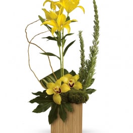 Yellow lilies and orchids arranged in a tall wooden container