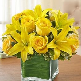 Yellow roses and lilies arranged in a square glass vase