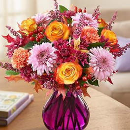 Mixed bouquet of orange roses and pink daisies in a purple vase