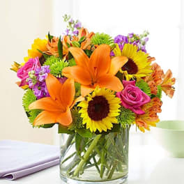Bright mixed bouquet with orange lilies, sunflowers, and pink roses in a glass vase