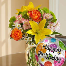 Bouquet of yellow lilies and orange roses in a glass vase with a birthday balloon
